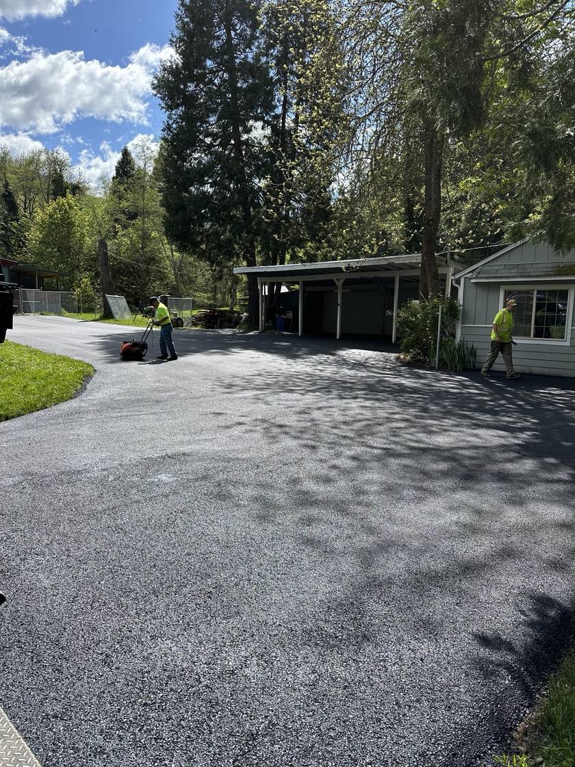 Workers finishing an asphalt driveway beside a home and carport.