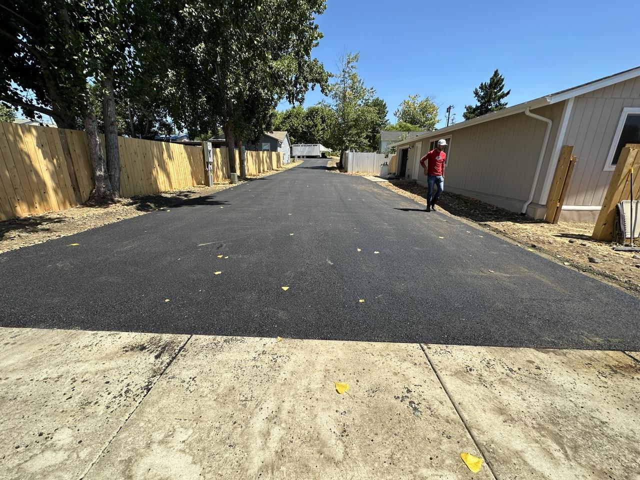 Wide black asphalt drive alongside a home and wooden fence.