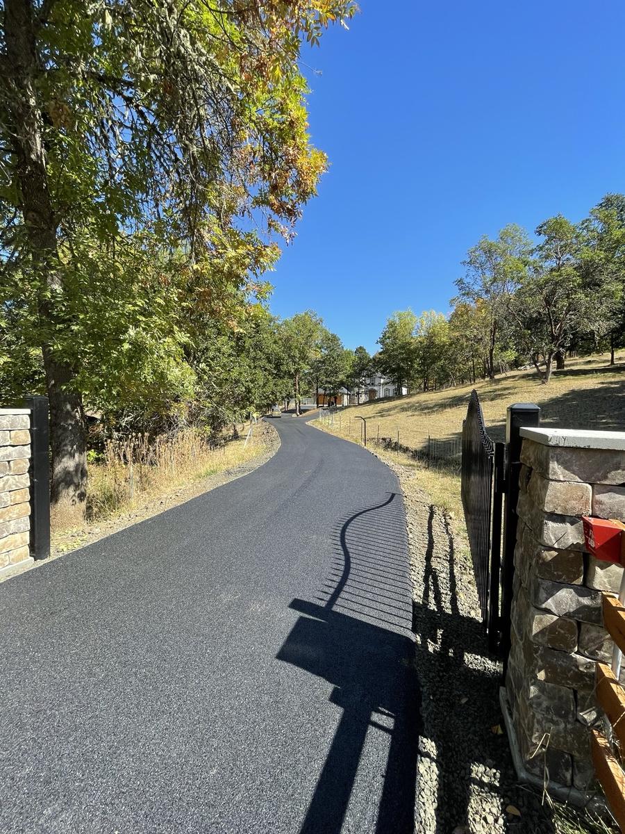 Black asphalt driveway winding through a stone gateway toward a home.