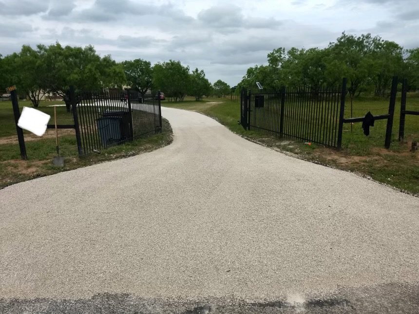Light-colored chip seal entrance extending through open black gates.