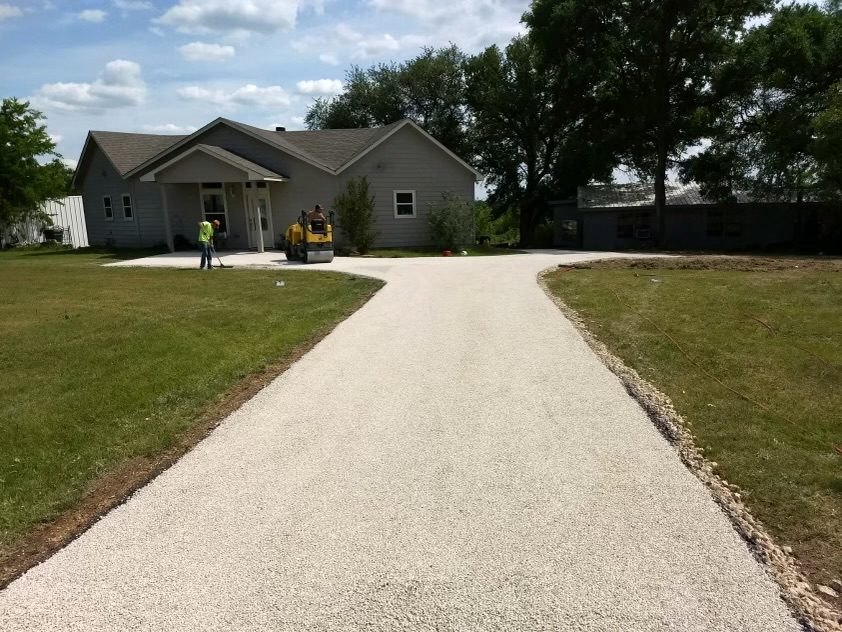 Roller and crew on a light-colored chip seal driveway in front of a home.