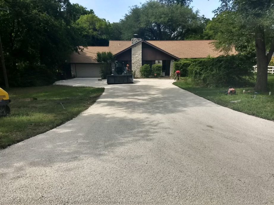 Crew and equipment on a chip seal driveway leading to a house.