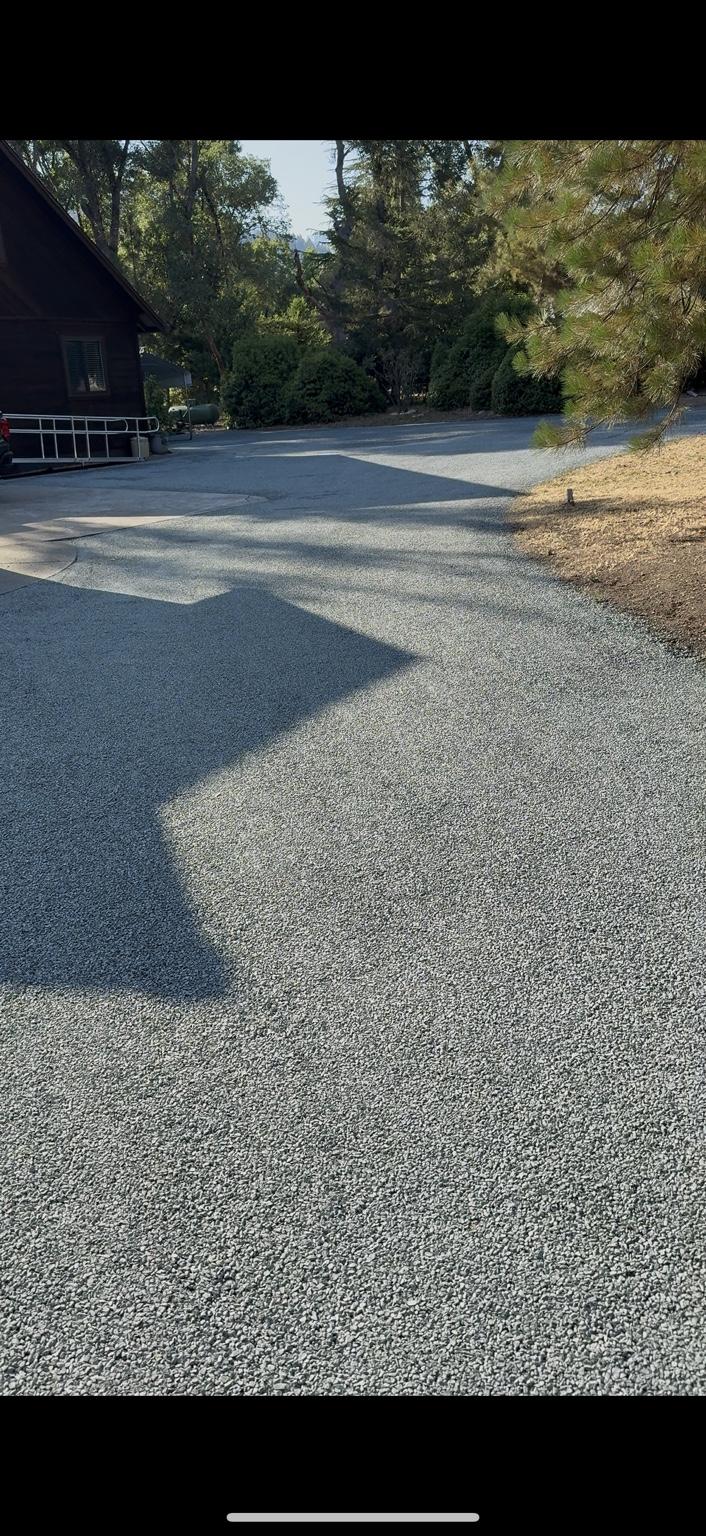 Gray chip seal driveway wrapping around a home beneath mature trees.