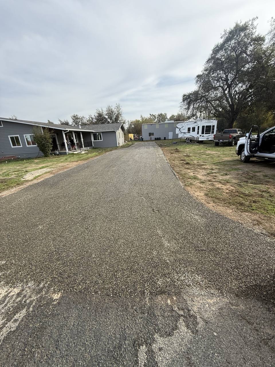 Chip seal driveway extending past a home toward a detached shop.